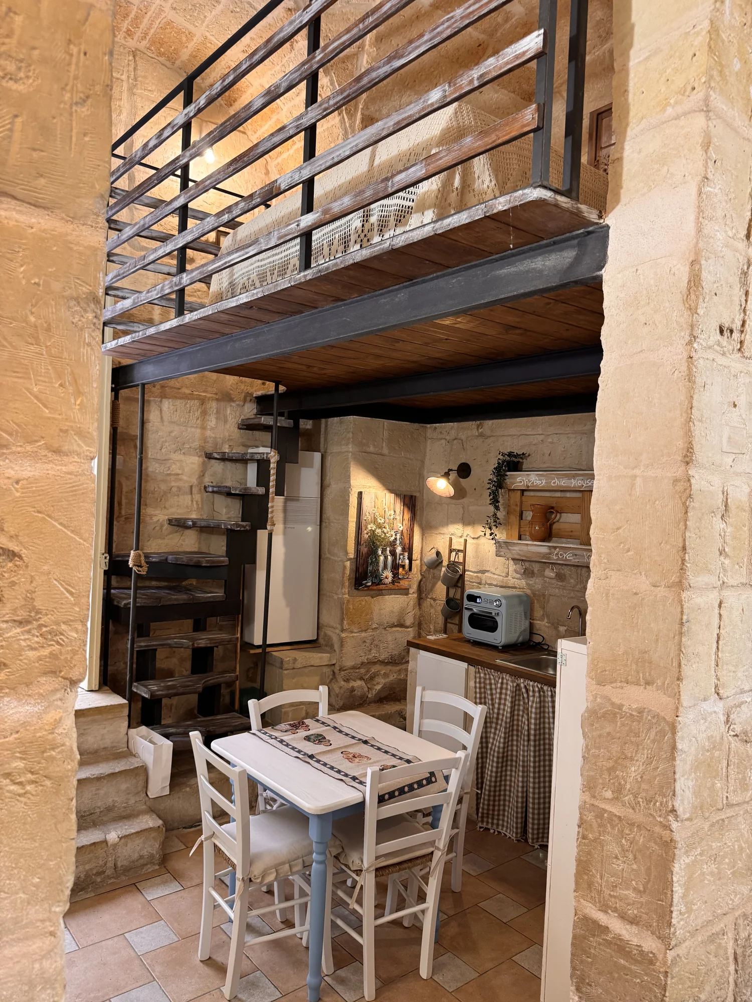 Zona pranzo e cucina sotto il soppalco, con scala a chiocciola e pareti in pietra di Boemondo House