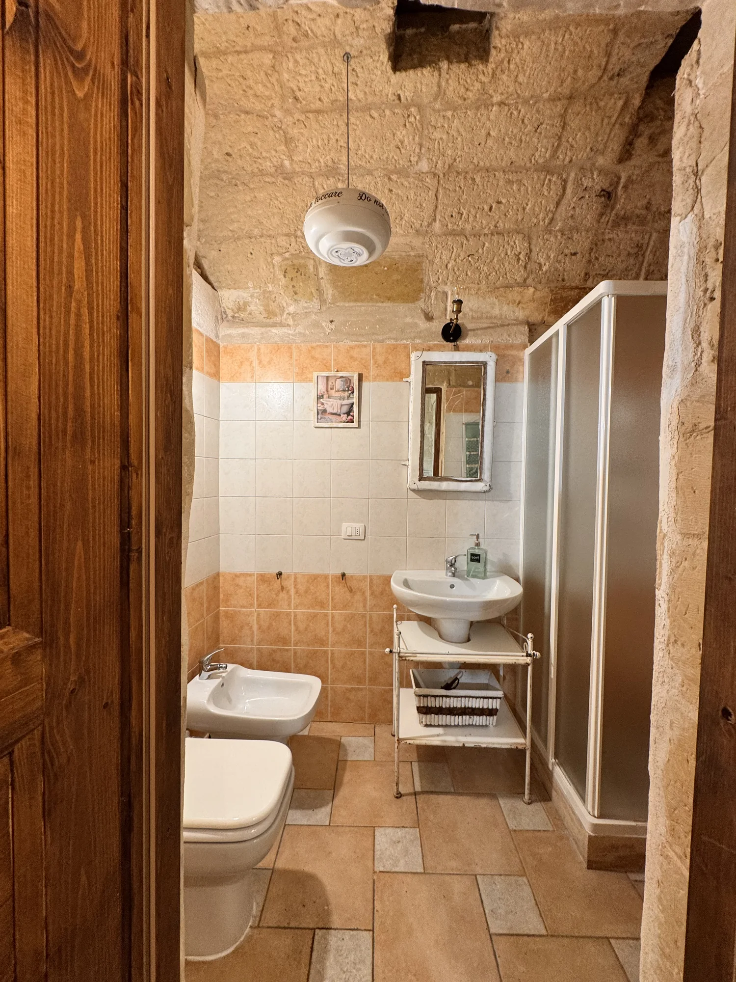 Bagno con lavabo e cabina doccia tra le pareti in pietra di Boemondo House