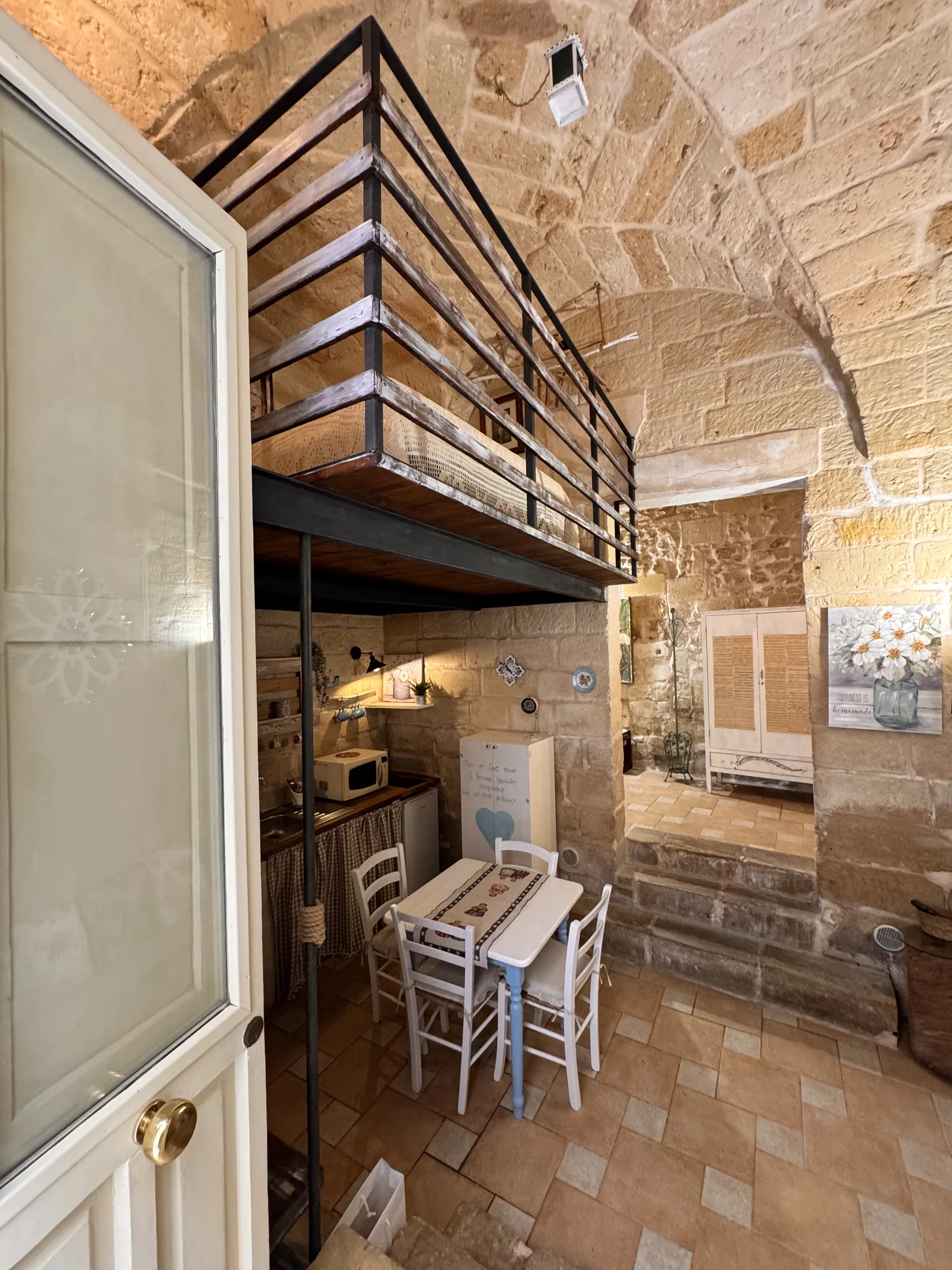 Cucina sotto il soppalco con pareti in pietra e scala in legno di Boemondo House
