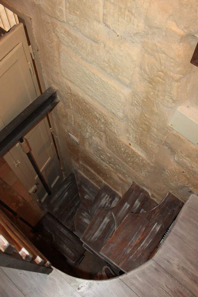 Scala a chiocciola in legno vista dall’alto, tra le pareti in pietra di Boemondo House